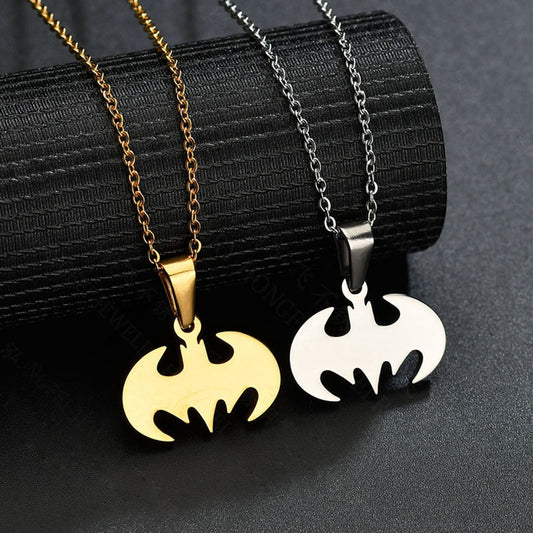 Ett Batman-inspirerat halsband i rostfritt stål med en guldfärgad och silverfärgad plätering, liggandes på en svart texturerad bakgrund.